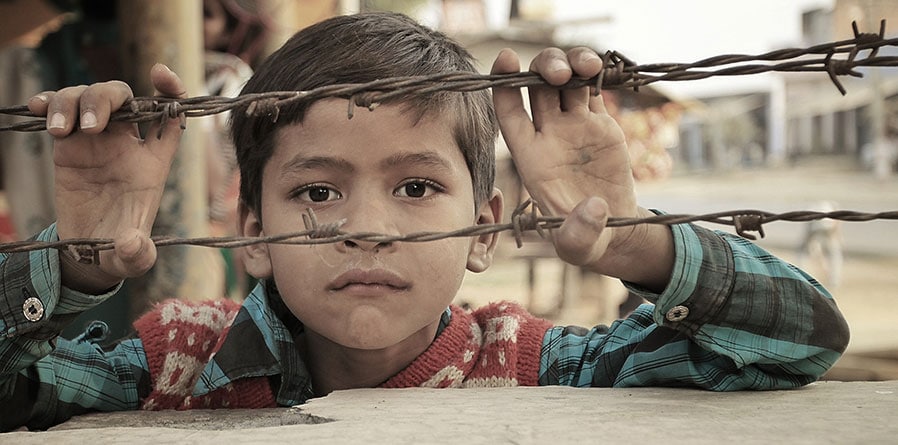 A young boy gazes through a barbed wire fence, his curious eyes filled with longing and innocence.