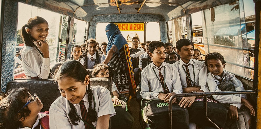 School children on a bus, excitedly chatting and looking out the windows, on their way to school.